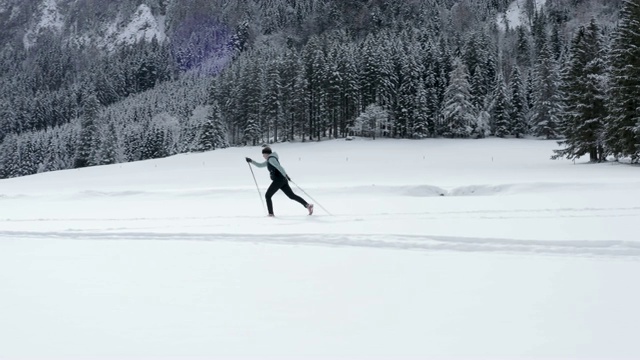 无人机拍摄的一名年轻女子在群山环绕的雪谷中越野滑雪视频素材