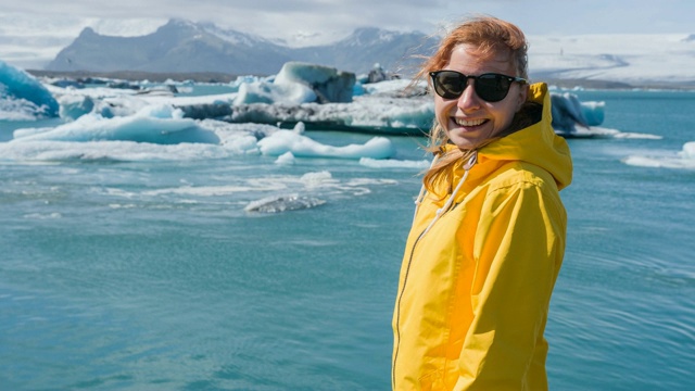 微笑的女人正在欣赏冰岛的Jokulsarlon冰川湖，上面有冰山和海鸟视频素材