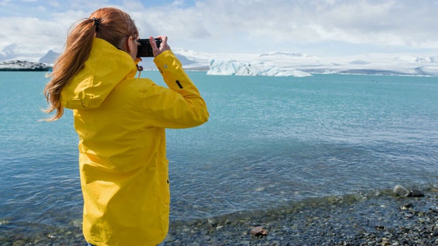 一名女游客在冰岛的钻石海滩上，拍摄从Jokulsarlon冰川泻湖上漂浮的冰山视频素材