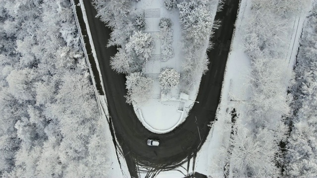 鸟瞰图转向公路在山区冬季积雪覆盖森林视频素材