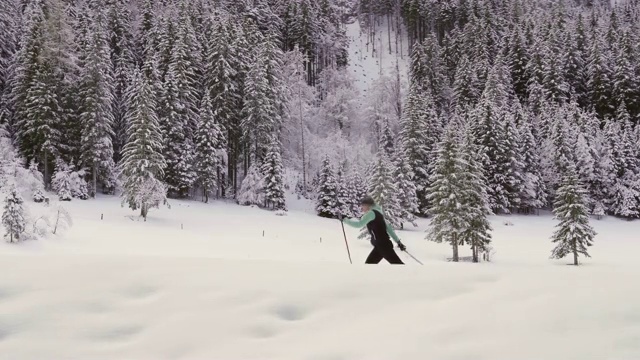 下面是一名年轻女子在被群山包围的雪谷中越野滑雪的镜头视频素材