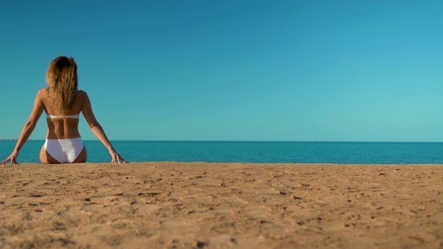 那个穿着白色泳衣的漂亮女孩坐在以大海为背景的地方视频素材