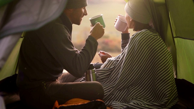 两个男人和女人早上在帐篷里喝热茶。情侣一起旅行的概念。视频素材