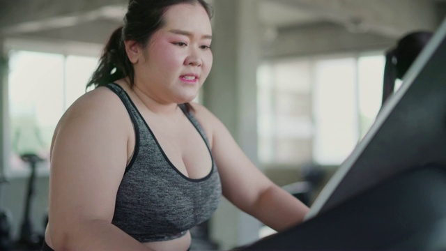 超重女性在跑步机上进行有氧运动在健身房里进行锻炼。视频素材