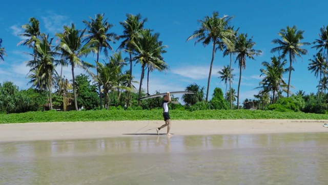 带着冲浪板的冲浪者在沙滩上行走，背景是棕榈树视频素材