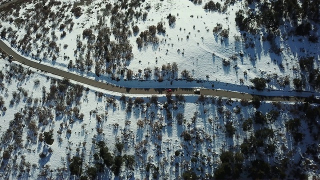 在恶劣天气下，俯视图无人机在弯曲的道路、风山和覆盖着积雪的森林上空飞行。视频素材