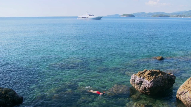 年轻女子浮潜在蓝色的热带水域穿着红色泳衣与游轮在地平线。旅游的概念视频素材