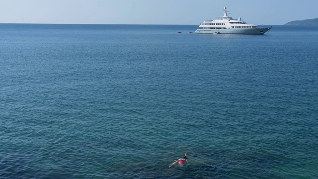 年轻女子浮潜在蓝色的热带水域穿着红色泳衣与游轮在地平线。旅游的概念视频素材