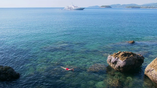 年轻女子浮潜在蓝色的热带水域穿着红色泳衣与游轮在地平线。旅游的概念视频素材