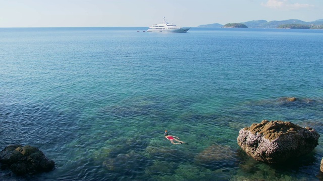 年轻女子浮潜在蓝色的热带水域穿着红色泳衣与游轮在地平线。旅游的概念视频素材