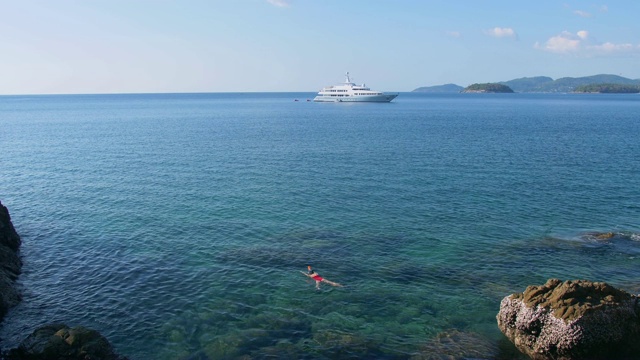 年轻女子浮潜在蓝色的热带水域穿着红色泳衣与游轮在地平线。旅游的概念视频素材