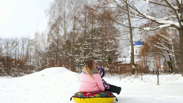 快乐的妈妈和女儿在冬天的雪地里玩雪橇和打雪仗。母亲和孩子笑和高兴滑翔在一个充气管。圣诞节期间全家游玩公园。慢动作视频素材