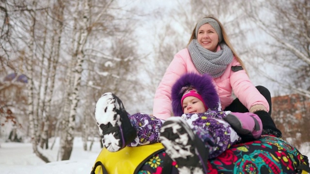 快乐的妈妈和女儿在冬天的雪地里玩雪橇和打雪仗。母亲和孩子笑和高兴滑翔在一个充气管。圣诞节期间全家游玩公园。慢动作视频素材