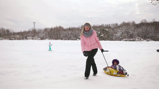 快乐的妈妈和女儿在冬天的雪地里玩雪橇和打雪仗。母亲和孩子笑和高兴滑翔在一个充气管。圣诞节期间全家游玩公园。慢动作视频素材