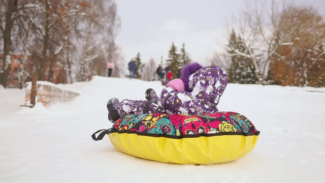 快乐的妈妈和女儿在冬天的雪地里玩雪橇和打雪仗。母亲和孩子笑和高兴滑翔在一个充气管。圣诞节期间全家游玩公园。慢动作视频素材