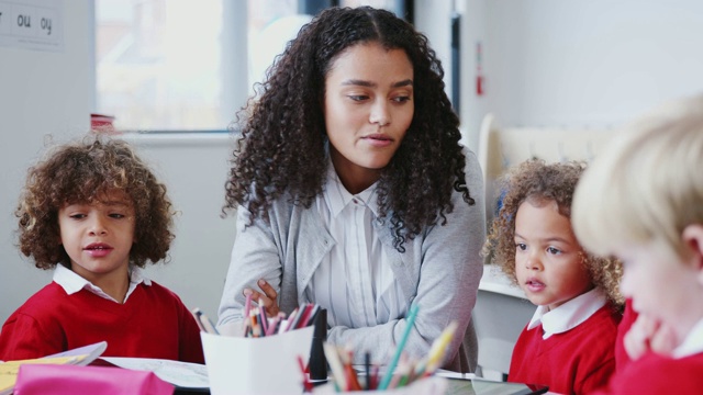 微笑的女幼儿学校老师坐在桌子上的学生，腰部以上视频素材