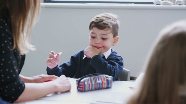 一名女教师与小学生坐在一起上小学课，选择性地集中注意力视频素材