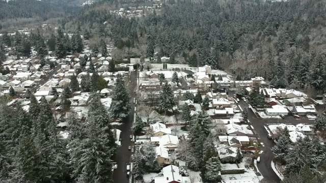 住宅区上空鸟瞰图。向上倾斜，可以看到附近的街道和被雪覆盖的树林。视频素材