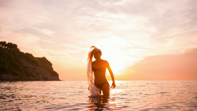 身穿比基尼的女子在夕阳下站在海水中向后拨弄头发，在海滩上享受暑假视频素材