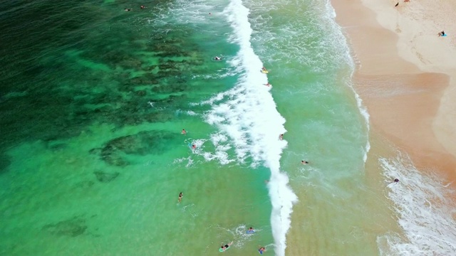 空中:绿色海洋，温和的海浪和沙滩与冲浪者从远处视频素材