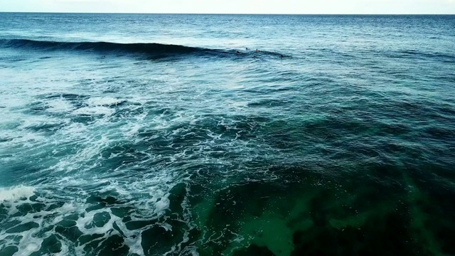 鸟瞰图:清澈的蓝色海洋与波浪形成和冲浪者等待在水视频素材