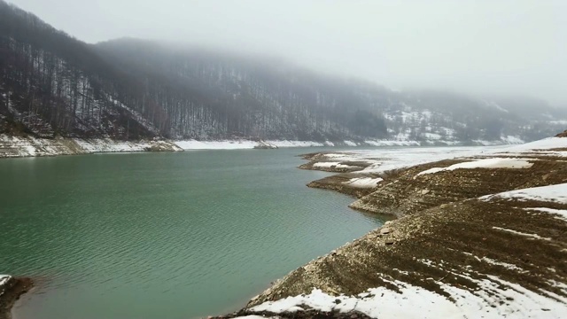 冬天的景色，湖面在山上，白雪覆盖的海岸显示出层层的砾石和薄雾森林在背景视频素材