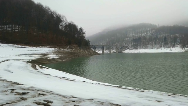 冬天的景色，山上静静的湖面，白雪覆盖的海岸和森林在雾，雾天的背景视频素材