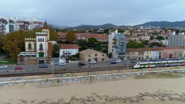 航拍俯视图运行的火车，汽车的道路和海边高速公路与十字路口靠近马努海滩，蒙哥马利，西班牙巴塞罗那。傍晚天空有云。视频素材