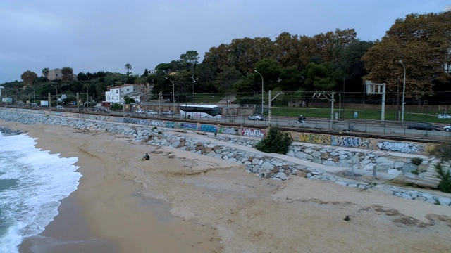 航拍俯视图运行的火车，汽车的道路和海边高速公路与十字路口靠近马努海滩，蒙哥马利，西班牙巴塞罗那。傍晚天空有云。视频下载