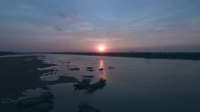 空中:飞回来，夕阳下河边有一座竹桥，游来游去的人影视频素材