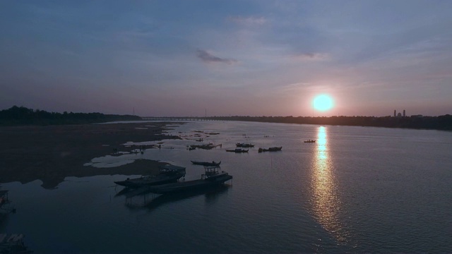 空中:飞回来，夕阳下的江边有一座竹桥，船边游人的剪影视频素材