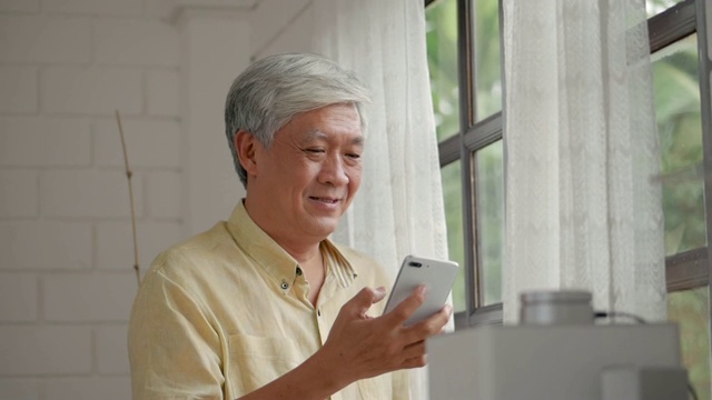 资深亚洲人谈论智能手机愉快和微笑旁边的窗户在家里。慢动作视频素材