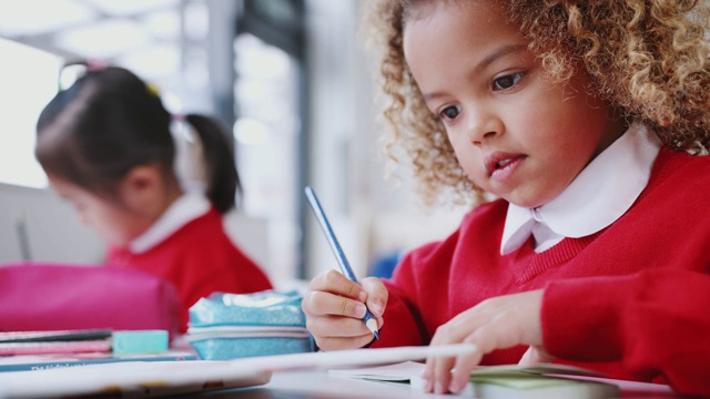 近距离的混合种族女学生坐在一个幼儿学校教室的书桌上画画，低角度视频素材