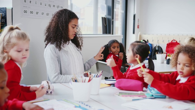 年轻的女幼儿教师坐在一张桌子在一个班和她的学生，数女孩视频素材