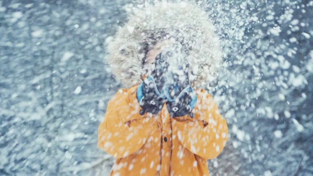 男孩穿着温暖的兜帽休闲皮大衣外套外套看向相机和拍与雪满手掌与飘落的雪背景。户外时间和冬季服装概念视频。视频素材