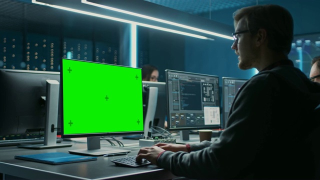 在数据中心系统控制室的桌面绿色模拟屏幕计算机上工作的聪明男性IT程序员。年轻的专业人员编程复杂的代码团队视频素材