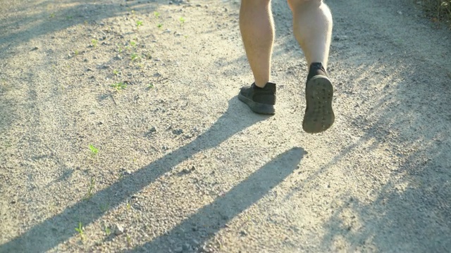 夏天的一天，一个穿着短裤和黑色运动鞋的男人走在一条土路上。视频素材