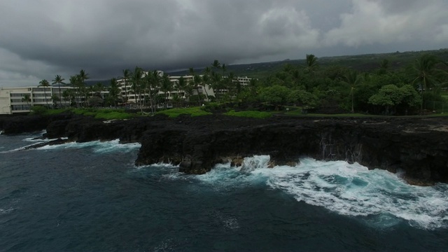 天线:海浪拍打着高高的，岩石海岸上有建筑物和棕榈树视频素材