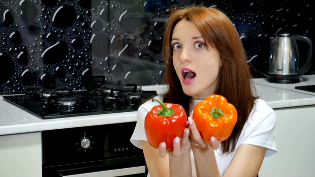 年轻的黑发妻子在厨房准备食物前用蔬菜盖住眼睛，摆弄着红色和橙色的青椒。健康的生活方式和节食观念视频素材
