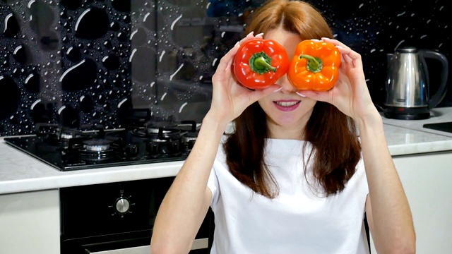 快乐兴奋的年轻女子玩红色和橙色的青椒覆盖她的眼睛在厨房准备食物。视频素材