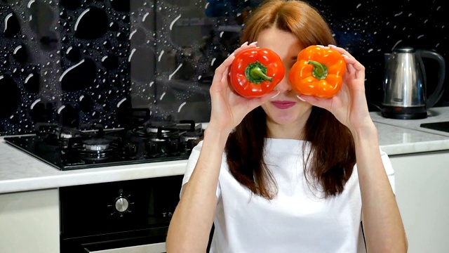 迷人兴奋的年轻女模特在厨房准备食物之前，用红色和橙色的青椒盖住她的眼睛。视频素材