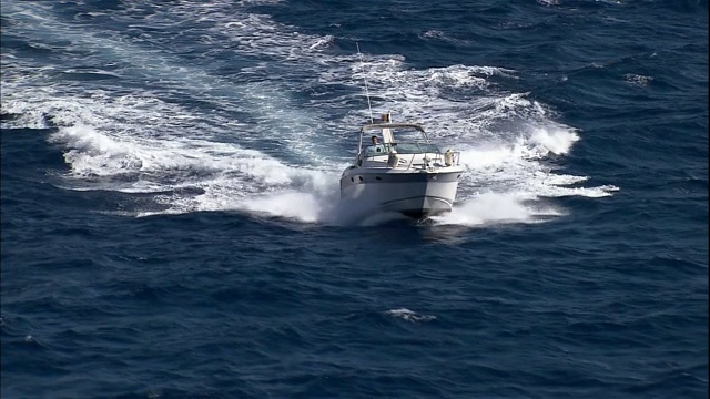 一艘快艇在一个沿海村庄附近波涛汹涌的海面上巡航。视频素材