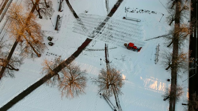 小型红色拖拉机清理城市公园广场，空中积雪视频素材