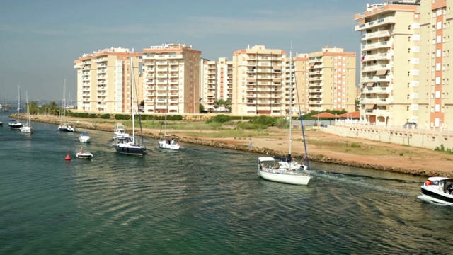 从Mar Menor laguna到地中海的吊桥上，一队帆船在航行。城市景观背景。晴朗的夏日，在拉曼加，穆尔西亚，Catragena，西班牙。视频下载