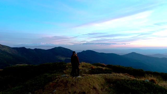 一个男人和一个女人站在山顶上以夕阳为背景视频素材