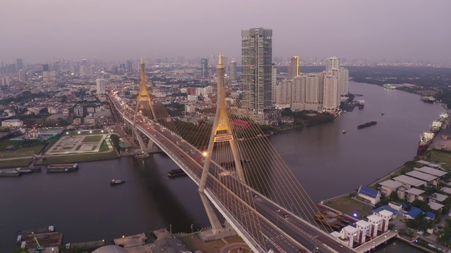 无人机镜头鸟瞰图，普密蓬悬索桥横跨曼谷市湄南河，在日落天空和云彩在桥上的汽车在泰国曼谷。视频素材