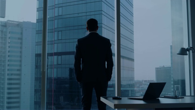 Back View of the Thoughtful Businessman wearing a Suit Standing in His Office, Hands in Pockets and considering Next Big Business Deal, Looking out of the Window.(后视图)大城市商业区全景窗景。视频购买