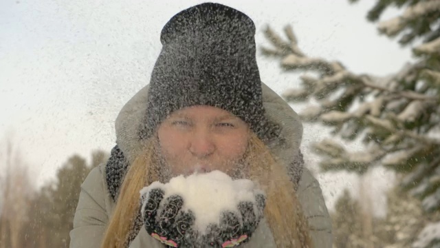 快乐的小女孩用冬天的衣服从手中吹雪背景视频素材