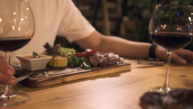 在烧烤餐厅晚餐时，手持酒杯的男性。人们在烧烤餐厅吃烤牛排视频素材