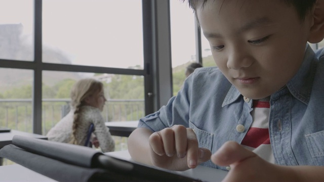 可爱的男孩在桌子上滚动电子平板电脑视频素材